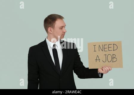 Un disoccupato con un cartello con la frase i Need A Job su sfondo grigio chiaro Foto Stock