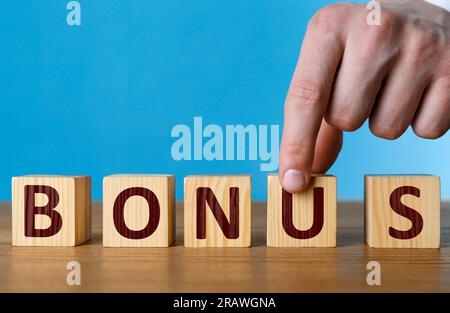 Uomo che fa parola Bonus di cubi con lettere su un tavolo di legno, primo piano Foto Stock