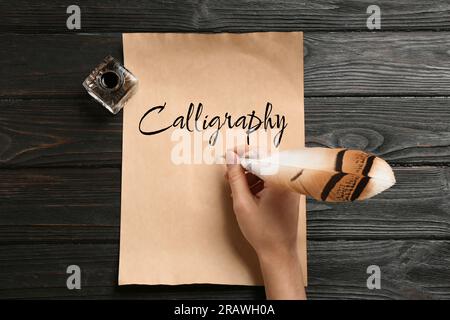 Donna che scrive calligrafia con piume e inchiostro su pergamena su un tavolo di legno, vista dall'alto Foto Stock