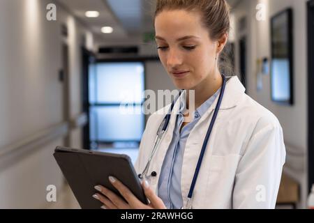 Medico femminile caucasico che indossa l'uniforme medica usando la compressa all'ospedale. Ospedale, comunicazione, medicina e servizi sanitari, inalterati. Foto Stock