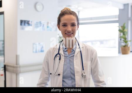 Ritratto di medico femminile caucasico felice che indossa uniforme medica e stetoscopio in ospedale. Ospedale, medicina e servizi sanitari, inalterati. Foto Stock