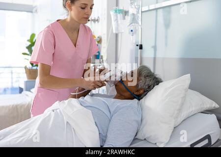 Medico femminile diversificato e paziente anziano che indossa la maschera di ossigeno in ospedale. Ospedale, medicina e servizi sanitari, inalterati. Foto Stock