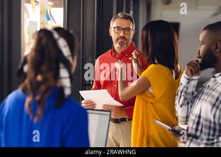 Persone d'affari diversificate che si occupano di riunioni, brainstorming e utilizzo del laptop in ufficio. Affari occasionali, lavoro di squadra, comunicazione e lavoro, inalterati. Foto Stock
