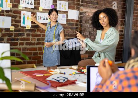 Felice e diversificato stilisti che utilizzano un tablet e discutono dei progetti in studio. Business, lavoro di squadra, comunicazione, riunione, brainstorming, moda e des Foto Stock