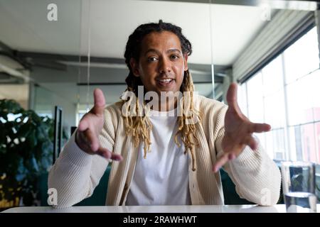 Felice uomo d'affari birazziale e informale in ufficio che effettua videochiamate, sorride e gesti. Lavoro, affari, comunicazione e ufficio informale, inalterato. Foto Stock