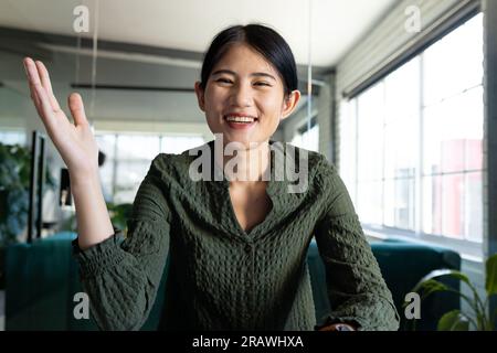 Donna d'affari asiatica e informale che ha videochiamate e gesti seduti alla scrivania in ufficio. Lavoro, affari, comunicazione e ufficio informale, inalterato Foto Stock