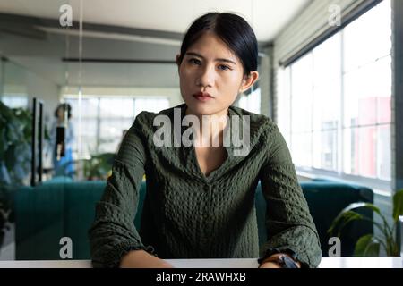 Donna d'affari asiatica informale che fa videochiamate e gesti seduti alla scrivania in ufficio. Lavoro, affari, comunicazione e ufficio informale, inalterato Foto Stock