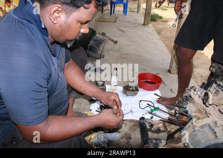 Il meccanico ripara un ciclomotore. Un uomo lavora come meccanico in un'officina di riparazione motociclistica locale. Odisha, India. Foto Stock