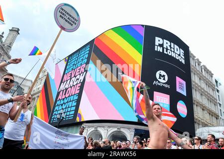 Londra, Regno Unito. I partecipanti alla sfilata Pride in London passano davanti allo spettacolo Piccadilly Lights, che mostra il tema di quest'anno, "Never Walk Alone". Foto Stock