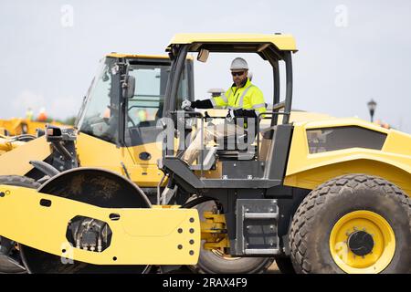 operaio impegnato in attrezzature edili. operaio edile che guida macchinari pesanti per lavori stradali. uomo che lavora in macchinari edili all'aperto Foto Stock