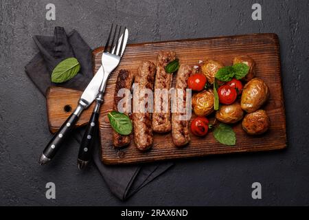 Deliziose salsicce alla griglia e patate su un asse di legno. Giacitura piatta Foto Stock