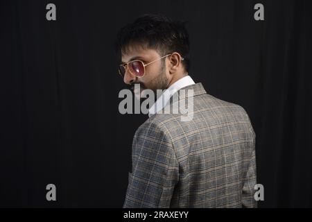 Ritrarre una persona vestita da lavoro felice in abito che indossa specifiche che mostrano stati d'animo diversi. Riprese a basso profilo di abbigliamento da ufficio barbuto. Sfondo nero Foto Stock