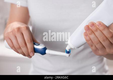 Donna che spreme dentifricio dal tubo allo spazzolino elettrico, primo piano Foto Stock