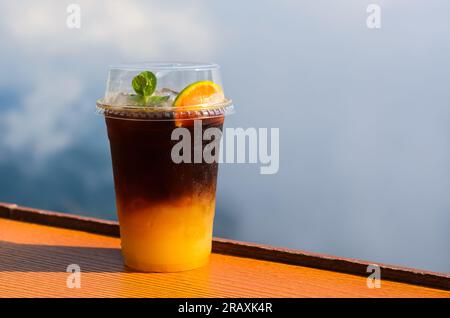 Un bicchiere di caffè ghiacciato si mescola con succo d'arancia messo sul tavolo con cielo e sfondo nuvoloso. Concetto di drink estivo. Foto Stock