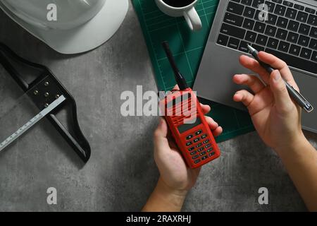 Sopra la vista del tecnico tecnico ingegnere industriale che tiene in mano il walkie talkie e utilizza il computer portatile sulla scrivania Foto Stock