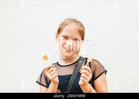 Ritratto all'aperto di una bambina carina che tiene caramelle lecca-lecca a forma di cuore Foto Stock