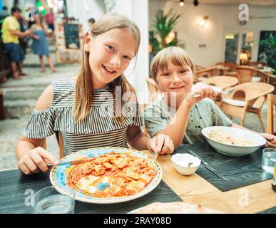 Due bambini divertenti che pranzano al ristorante, mangiano ravioli e pasta Foto Stock