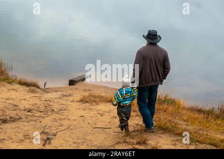 Una felice famiglia di due persone si trova in una nuvolosa giornata autunnale sulla riva del lago Foto Stock