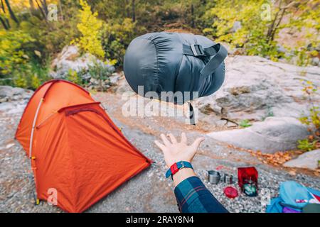 Borsa a compressione piccola e leggera con sacco a pelo in piuma sullo sfondo di una tenda in campeggio e varie attrezzature e oggetti da campeggio Foto Stock