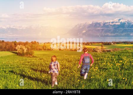 Due bambini, fratellino e sorella maggiore, che giocano insieme nei campi svizzeri con vista sul lago di Ginevra e sulle montagne francesi dell'alta Savoia. Immagine t Foto Stock