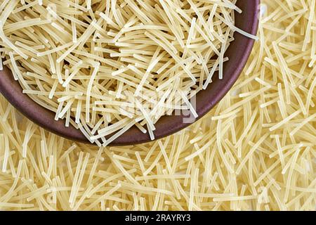 Spaghetti alle uova, pasta, in una ciotola di ceramica marrone e sparsi intorno isolato su fondo bianco. Vista dall'alto con spazio di copia Foto Stock