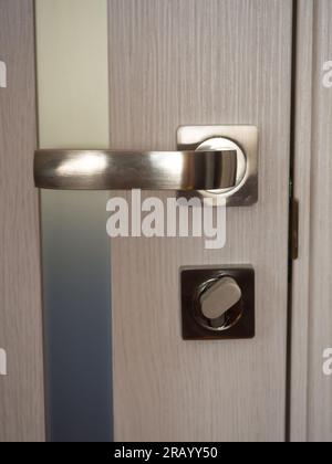 Primo piano delle porte interne beige con inserti in vetro smerigliato. Elegante maniglia della portiera cromata color argento con serratura sulla portiera interna moderna. Concetto di CA Foto Stock