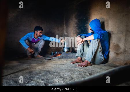 28 giugno 2023, Nagthat, Uttarakhand, India. Due giovani che preparano tè al latte in una stufa di argilla o chulha all'interno di una casa di fango. Soggiorno a casa a Uttarakhand, Foto Stock