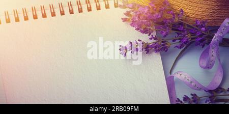 Libro vuoto con fiori estivi e un cappello di paglia sullo sfondo, spazio per copiare. Base piatta con spazio per la copia Foto Stock