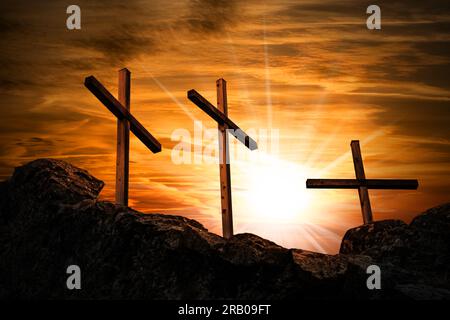 Silhouette di tre croci religiose in legno sopra la collina contro un cielo spettacolare e raggi del sole al tramonto o all'alba. Simbolo religioso del venerdì Santo. Foto Stock