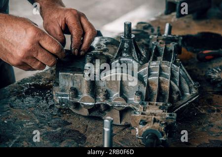 Riparazione meccanica cambio su banco di lavoro in metallo in officina. Meccanico automatico al lavoro. Flusso di lavoro autentico. Mani da vicino. Foto Stock