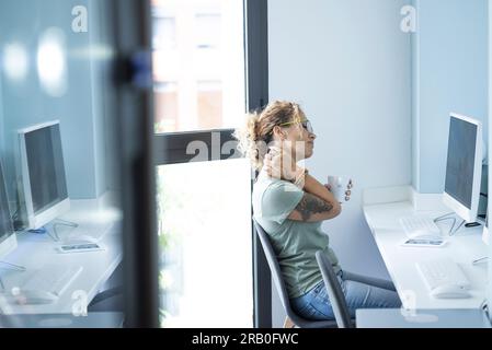 Lavoratrice stanca seduta alla scrivania massaggiando collo e spalle per un lavoro eccessivo sulle attività online. Cattiva postura dolorosa. Donne stressate solo sul posto di lavoro in ufficio. Uso eccessivo del computer Foto Stock