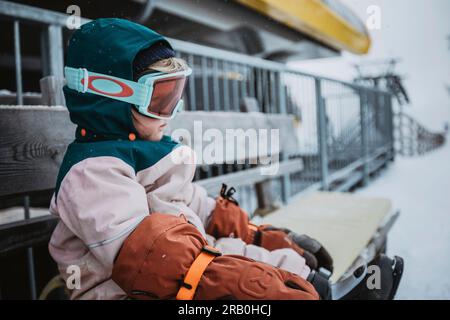 Una bambina in tuta da sci con occhiali da sci siede su una panchina Foto Stock