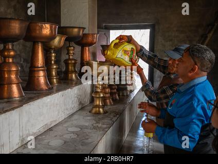 Pellegrini che mettono olio nelle lmaps del petrolio nel monastero di Shey, Ladakh, Shey, India Foto Stock
