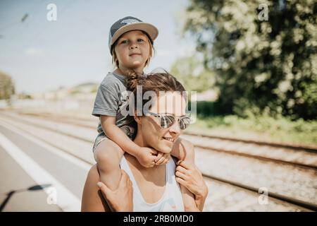 La madre porta il figlio sulla spalla su una piattaforma del treno Foto Stock