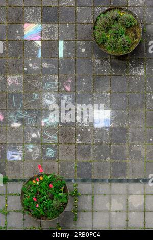 Disegni per bambini dal gesso in un cortile con vasi di fiori. Foto Stock