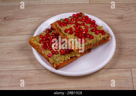 Semi di melograno di avocado Toasties in piatto bianco su sfondo di legno Foto Stock