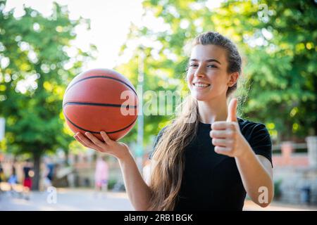 Un giocatore di basket con un pallacanestro in mano mostra i pollici in alto sorridendo Foto Stock