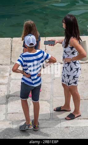 madre e due bambini al mare in una calda giornata di sole in croazia, madre e bambini alla moda, vacanze estive, signora elegante con bambini in vacanza. Foto Stock