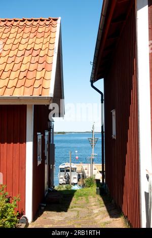 Vicoli stretti e case rosse con angoli bianchi nel villaggio rurale di pescatori nell'arcipelago di Stoccolma, affittando una barca ormeggiata al molo in estate svedese Foto Stock