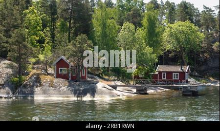 Due cottage svedesi di vernice rossa vicino al bordo dell'acqua del lago forestale nel pittoresco paesaggio estivo scandinavo Foto Stock
