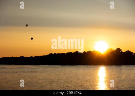 Caldo tramonto arancione sull'acqua nell'arcipelago di Stoccolma in estate con tre mongolfiere nel cielo Foto Stock