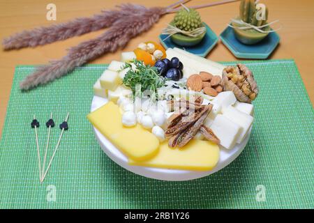 Delizioso mix di formaggi con uva, marmellata, snack, cracker, noci e vite su un asse di legno. Concetto di cena o aperitivo. Squisito piatto di formaggi, vino Foto Stock