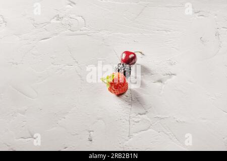 Tre piccoli frutti di bosco maturi su una superficie bianca Foto Stock