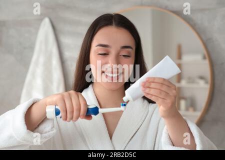 Una giovane donna che spreme dentifricio dal tubo allo spazzolino elettrico in bagno Foto Stock