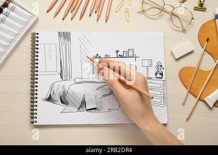 Donna che disegna l'interno della camera da letto in un notebook con matita su un tavolo di legno, vista dall'alto Foto Stock