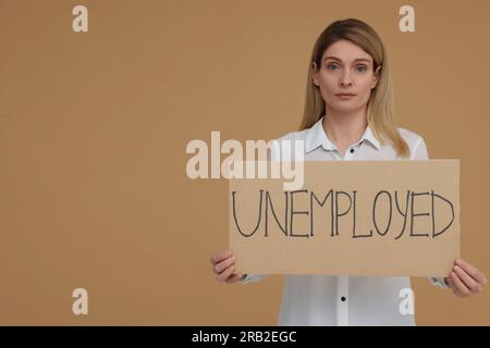 Donna con un cartello con la parola disoccupata su sfondo beige. Spazio per il testo Foto Stock