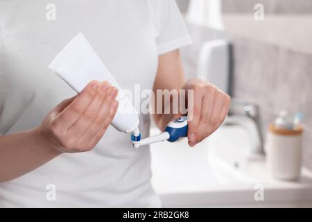 Donna che strizza dentifricio dal tubo allo spazzolino elettrico in bagno, primo piano Foto Stock