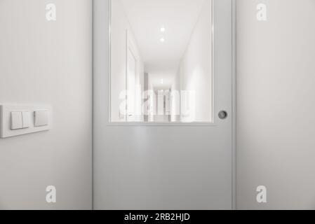 Corridoio di una casa con pareti lisce dipinte di bianco, porte laccate bianche con finestre in vetro e interruttori di luce dello stesso colore Foto Stock