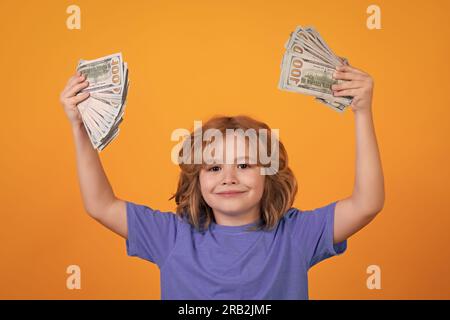 Ragazzino che mostra banconote da dollari, sogna di ricchi sullo sfondo isolato di uno studio giallo Foto Stock