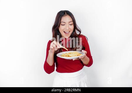 Immagine di una giovane ragazza asiatica sorridente che mangia patatine fritte isolate su sfondo bianco Foto Stock